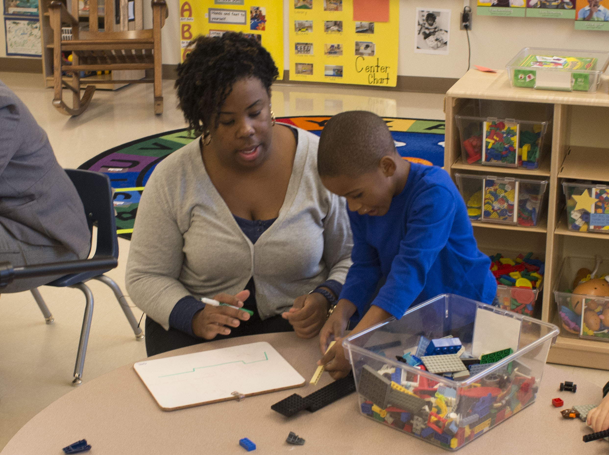 A teacher works next to a pre-K boy at a table